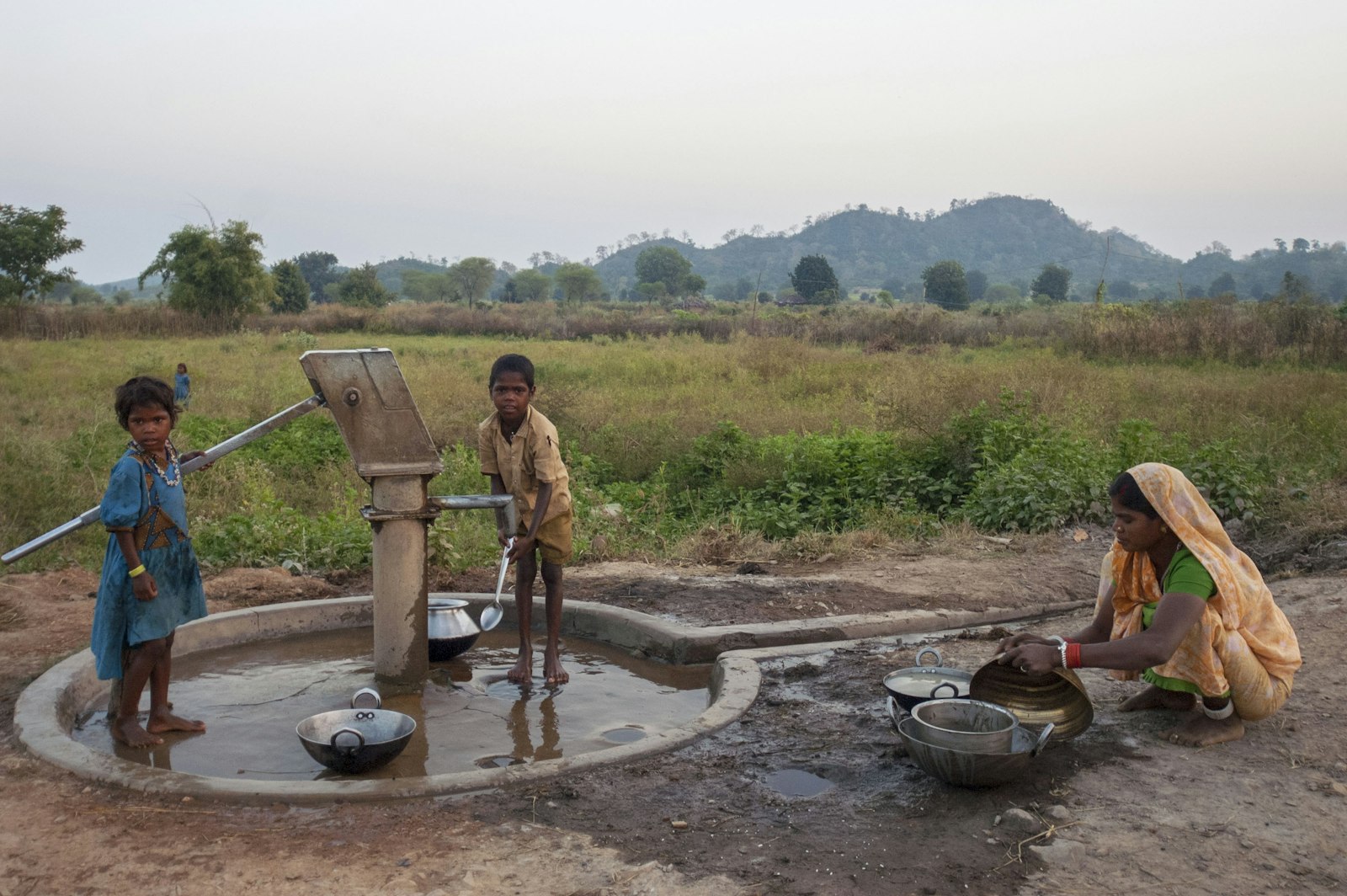 Children collecting water from an open handpump in an unserved village — the everyday reality this programme is built to change